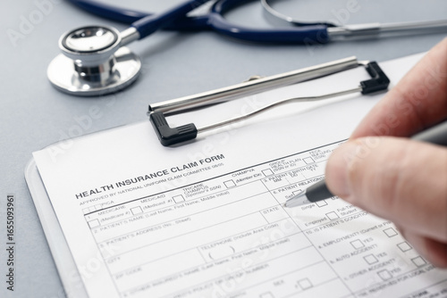 Hand filling on Health Insurance claim form and stethoscope on desk