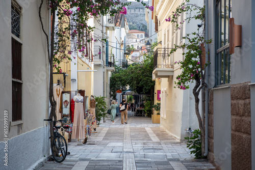 Fototapeta Naklejka Na Ścianę i Meble -  Narrow street within Nafplio, Greece, small shops, blooming flowers, and balconies, where people stroll leisurely