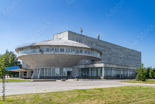 Technical university building in Ulyanovsk with a distinctive circular shape and concrete facade. Architectural structure in brutalist style under a clear blue sky surrounded by greenery.