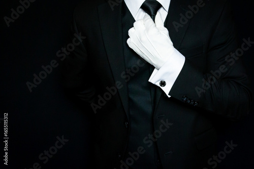 Formal Butler or Hotel Concierge in Dark Suit and White Gloves Straightening Tie. At Your Service.