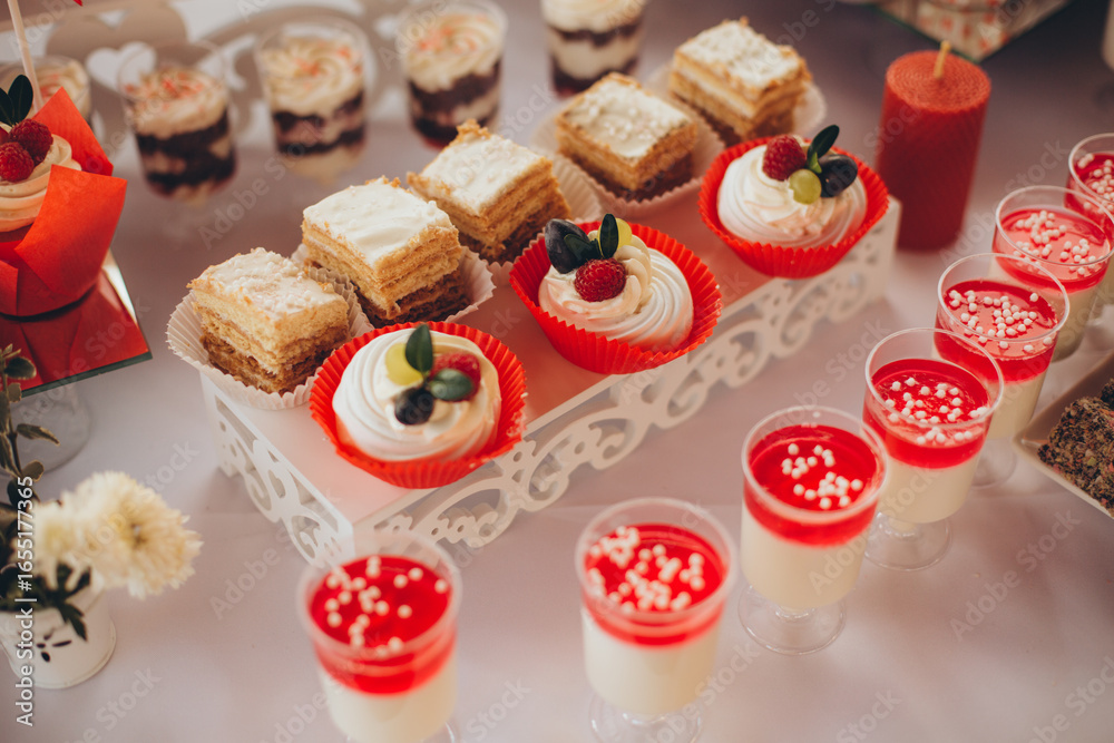 Naklejka premium Wedding candy bar with cake, desserts, fruits, and snacks, decorated in red and white colors for a festive celebration.