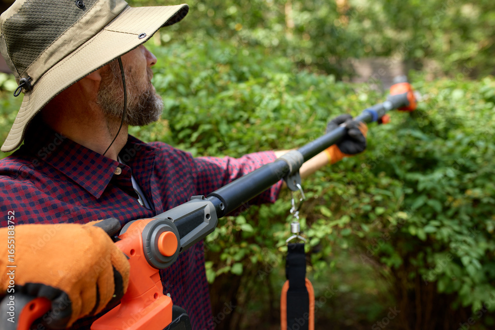 Fototapeta premium Man Using a Power Tool to Prune Bushes in a Garden Setting