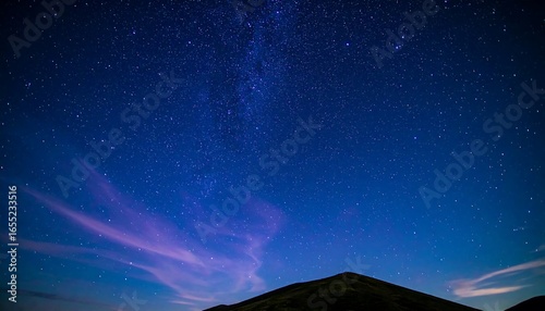 A breathtaking night sky, dotted with countless stars and a vibrant Milky Way, stretches above a silhouette of a mountain range.