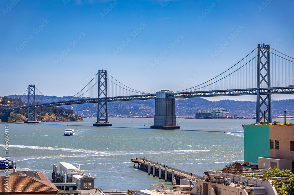 Obraz premium San Francisco Bay Bridge across the bay with a ferry boat on a bright sunny day