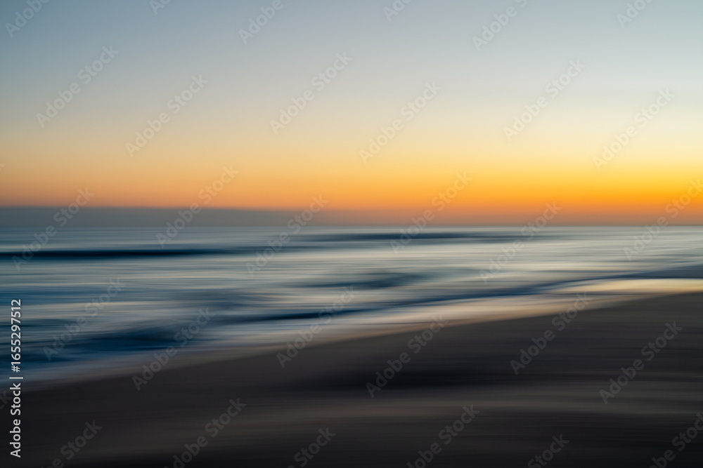Fototapeta premium Abstract blurred seascape with vibrant orange, purple, and blue hues during sunset.