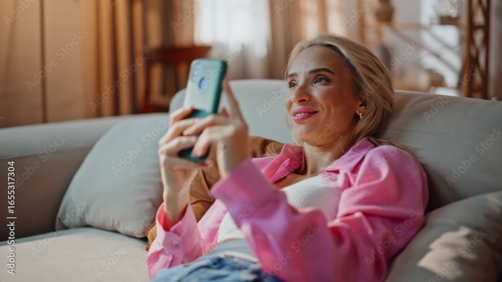 Fototapeta premium Reclining woman watching cellphone relaxing at soft sofa closeup. Dreamy girl