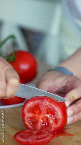 Woman cutting fresh red tomato with sharp knife on wooden cutting board in modern kitchen. Concept of healthy cooking, food preparation and fresh vegetable slicing for homemade meals. High quality 4k