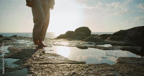 Barefoot woman walking on rocky shore with tide pools during golden hour