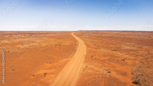 rone photography of the dirt road from Quilpie to bedourie. An aerial shot of a long, straight, unsealed dirt road cutting through a vast, flat, and arid red desert landscape under a clear blue sky.