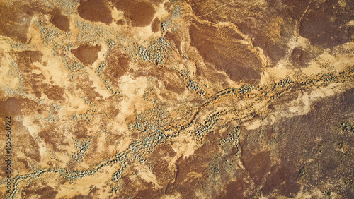 An aerial, abstract, top-down view of the ground in a desert landscape, showing textured patterns of light and dark. Drone photography of the desert inbetween Mount Isa and Boulia.