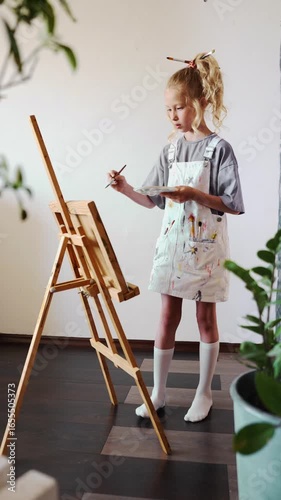 Full length of child painting at easel in cozy home studio, enjoying art as a hobby and part of creative learning. Concept of imaginative play and artistic skills development.