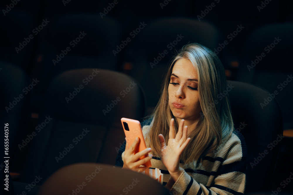 Naklejka premium Woman in a Movie Theater Checking her Phone Waiting for her Date. Bored single lady doom scrolling during a play in a theater 
