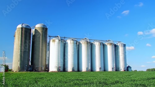 Silos stand tall against a blue sky, overlooking a field of lush green crops