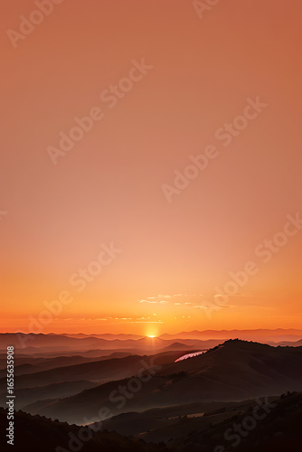 Sunrise over layered mountains, with a hazy orange sky and the sun peeking over the horizon.