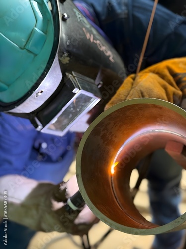 Industrial welder welding metal pipe with GTAW TIG torch, protective gloves, helmet, safety equipment, factory workshop, precision welding process, fabrication, repair, craftsmanship, heavy industry 