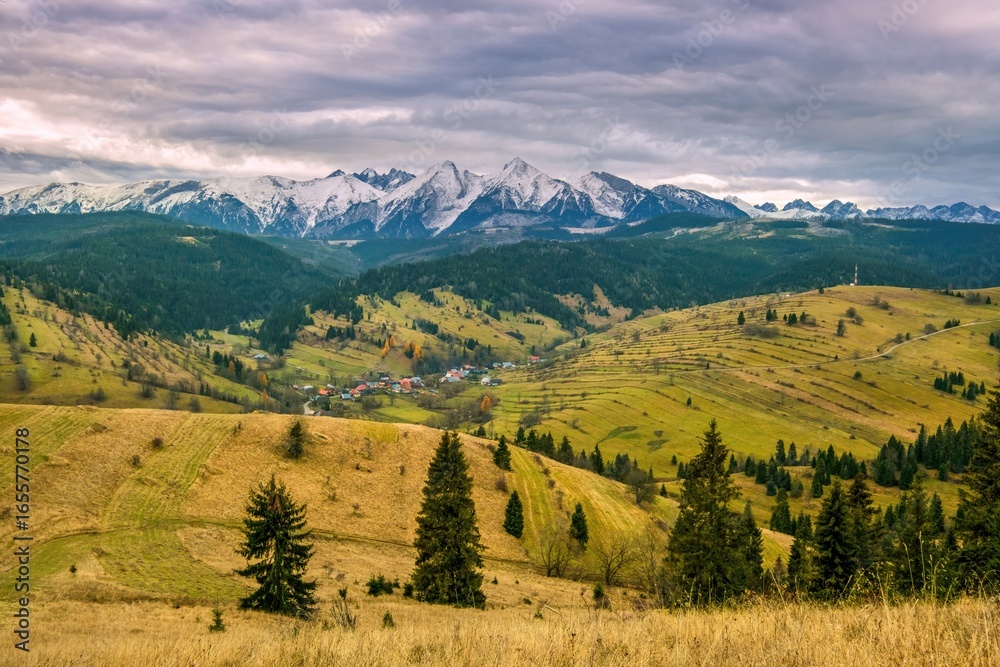 Obraz premium High Tatras autumn mountain valley. Autumn mountain village, with a beautiful autumn sun, snowy mountain peaks in the background. Mountain village in autumn landscape. Polskie gory