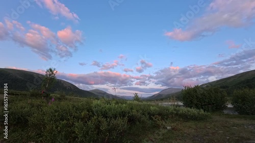 Sunset Time Lapse. Witness the beauty of a tranquil valley as clouds drift across the sky at dusk. Lush greenery frames the landscape, creating a peaceful moment in nature.