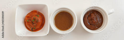Three small white bowls filled with different types of sauces on white background, top view