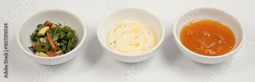 Three white bowls with salad, creamy sauce, and vinaigrette on white background