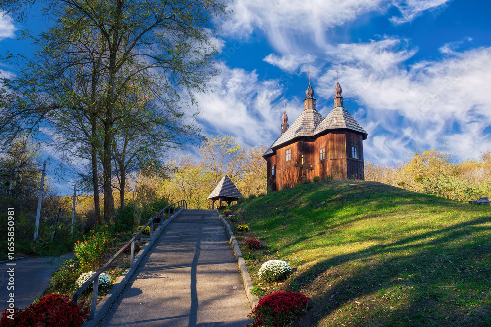 Obraz premium Wooden Cossack Church of Protection of Holy Mother of God rising on green hill in Monastyrok tract near Kaniv city in Cherkasy Oblast, Ukraine, on sunny autumn day with blue sky and white clouds