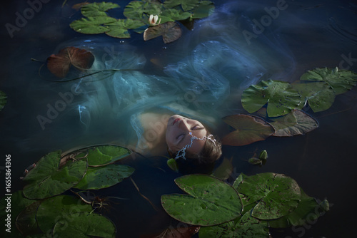 girl floats gracefully in a tranquil pond, partially submerged and surrounded by large lily pads. evening light casts a magical glow on her serene expression