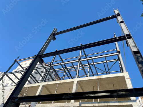 Tableau sur toile Steel frame structure of modern building under construction against blue sky - u