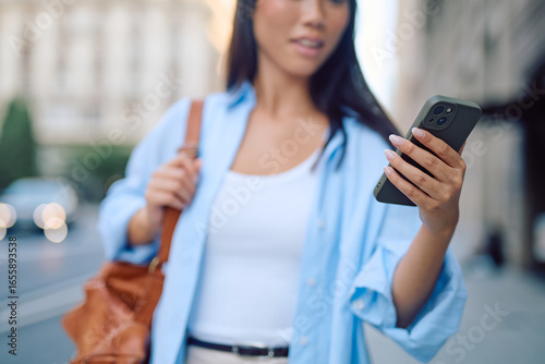Photography Asian businesswoman walking through an urban street, holding a smartphone and ch