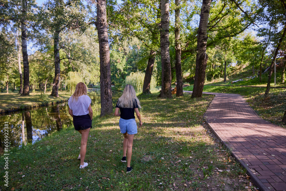 Fototapeta premium Two middle-aged sisters spending a summer morning in the park by a lake relaxing and having fun.