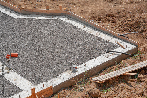 A newly poured concrete slab foundation and pathway, framed by wooden formwork and surrounded by loose gravel and brown soil on a sunny construction site.