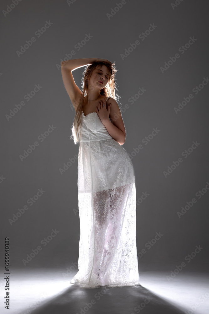 Fototapeta premium Elegant model posing in a white dress with dramatic lighting in a studio setting during a fashion shoot