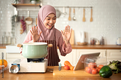Happy Muslim woman use digital tablet for live stream about cooking in modern Kitchen