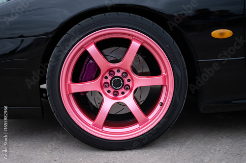 Detail of the front wheel on a JDM street racing and drift sports car, featuring a pink Gram Lights wheel and a modified black brake system