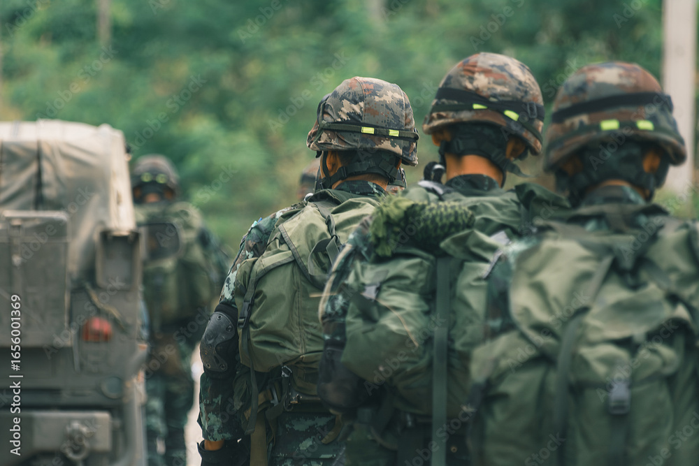 Fototapeta premium Group of soldiers wearing camouflage uniforms and helmets walking outdoors with military gear and backpacks during training or mission.
