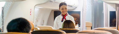 Smiling flight attendant greeting passengers in an airplane cabin, viewed from the seats, highlighting inflight service and comfort.