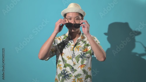 An Asian person wearing sunglasses and crossing arms with confident pose against a simple background, showing style, attitude, and modern lifestyle expression