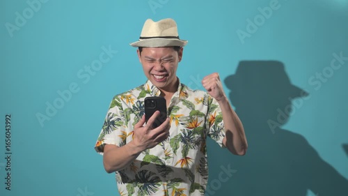 An Asian person looking at a phone and celebrating success with joy, captured against a simple background, expressing happiness and achievement in lifestyle content