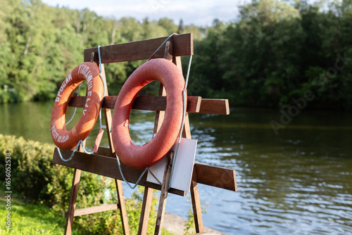 A vivid orange lifebuoy stands out against the serene marina backdrop, with luxury yachts moored nearby, evoking a peaceful coastal atmosphere on a cloudy day.