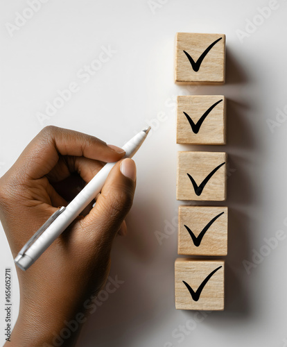 Hand holding white pen next to wooden blocks with black check marks task completion checklist concept productivity planning organization goal achievement business success.