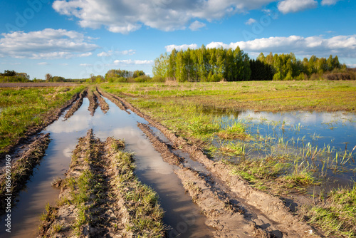 View of a dirt road and fields with water after rain