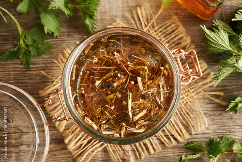 Fresh nettle root macerating in alcohol to prepare herbal tincture, top view