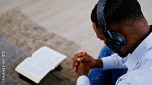 man praying with folded hands and headphones in front of a book – seamless loop

