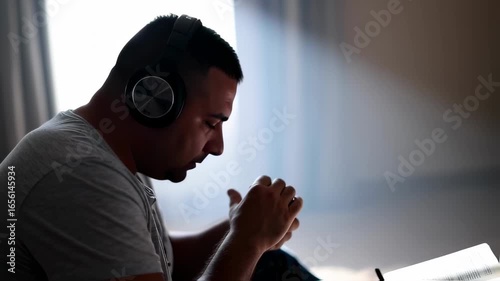 man praying with folded hands and headphones in front of a book – seamless loop
