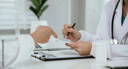 A doctor consults with a patient in a healthcare office, reviewing documents and providing medical advice, diagnosis, and treatment during a professional hospital or clinic appointment.