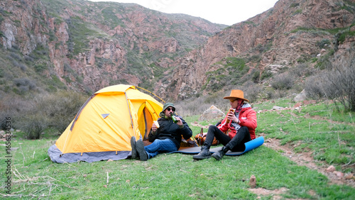 Fotografija A gay couple is sitting by a tent, eating sandwiches and drinking beer