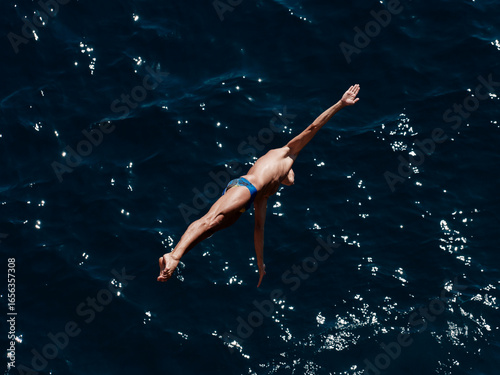 a professional male diver is jumping off a cliff into the sea