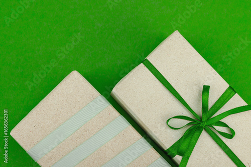 Eco-friendly gift boxes wrapped in kraft paper and decorated with satin ribbons on green background