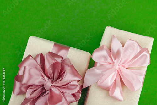 Eco-friendly gift boxes wrapped in kraft paper and decorated with satin ribbons on green background