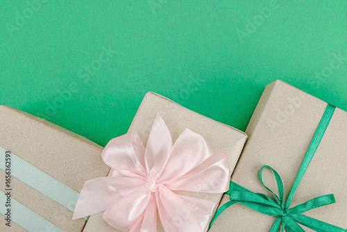 Eco-friendly gift boxes wrapped in kraft paper and decorated with satin ribbons on green background