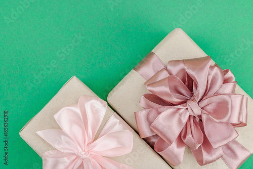 Eco-friendly gift boxes wrapped in kraft paper and decorated with satin ribbons on green background