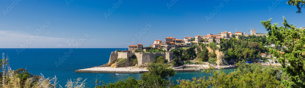 Obraz premium Panoramic view of Ulcinj’s historic Old Town with medieval stone walls, red-tiled roofs, and Adriatic Sea backdrop on a bright summer day.